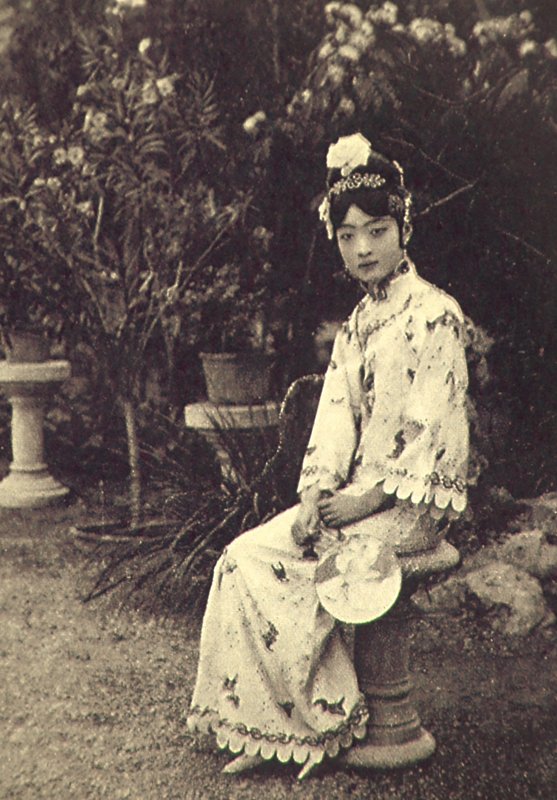 婉容端坐在花叢之中，她手中輕執團扇，憑添雅典嫵媚，髮髻間橫插著特製的〈珍珠髮簪〉，現藏瀋陽故宮。