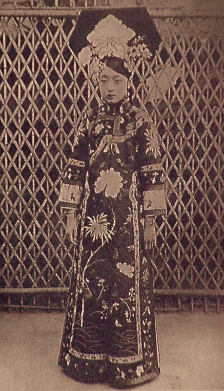婉容身著宮廷旗裝，展現「母儀天下」的端莊丰采。老照片上她手腕戴著精巧的手鐲飾品。那新潮的鏈飾或許透露內心的活潑與稚氣。照片上婉容所佩帶的〈銀製鏈式手鐲〉現藏瀋陽故宮。