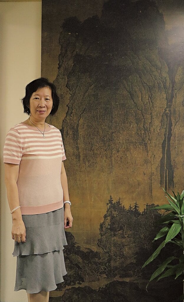 策展人台北故宮書畫處處長劉芳如，於辦公室范寬〈谿山行旅圖〉輸出圖前留影。攝影／鄭婷婷。