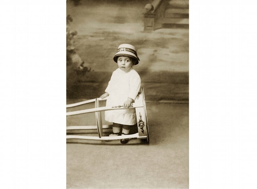佚名∣照相館人像照 攝影明信片 14x9cm 約1910年 私人收藏。圖∣高雄市立美術館。「小女孩的拍照姿勢其實尋常不過,但一個不協調的細節,隨即為整張照片添上怪異荒誕之感:為了讓幼兒不要亂動,居然讓她站在一個側倒的小圓桌之中。」