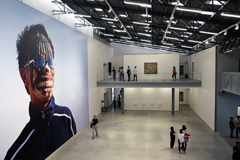 阿比查邦（Apichatpong Weerasethakul）將《原始計畫》（Primitive Project）中一名來自泰國東北、臉上配戴著鬼魂面具與太陽眼鏡的少年形象放大置於清邁當代美術館（MAIIAM Contemporary Art Museum）特展「阿比查邦：瘋狂的寧靜」（Apichatpong Weerasethakul: The Serenity of Madness）展廳中央，並做為特展的主視覺。（本刊資料室）
