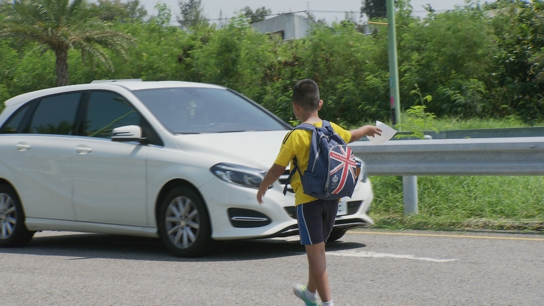 小小背包客心急趕不上下一個地點，手拿著搭便車的字條，便往馬路中間直直走去想要攔車，製作單位趕緊幫忙注意來往車輛，真是令人捏一把冷汗！