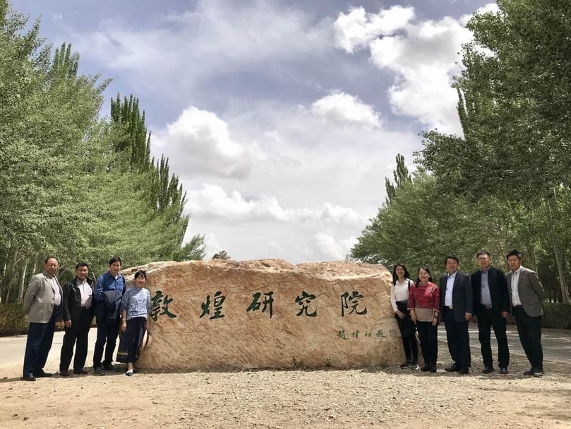 參訪代表團一行與敦煌研究院的副院長及單位主管於研究院入口合影。右起：馬鐵軍科長、程亮主任、張先堂副院長；左起：楊秀清研究員、宋真處長。（陸仲雁提供）