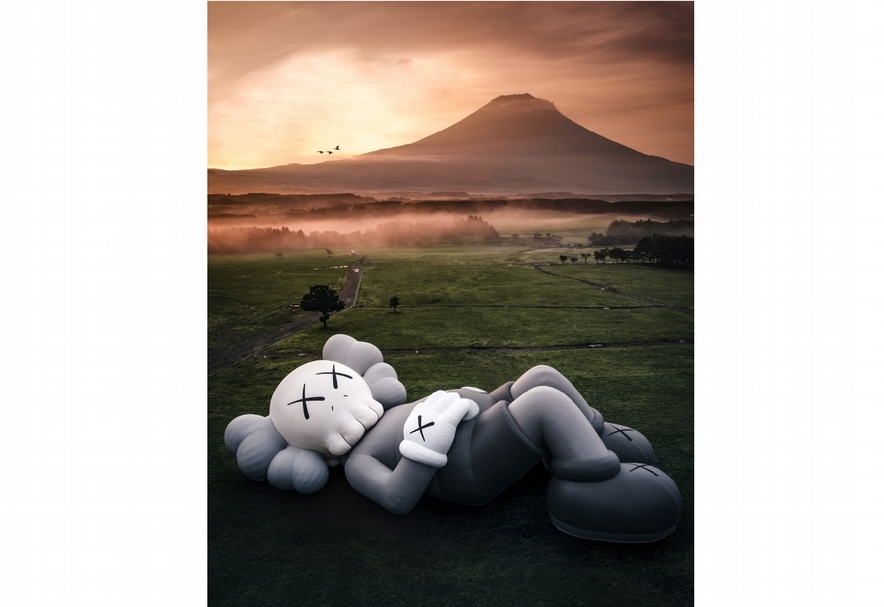 《KAWS：HOLIDAY》展覽現場，呈現KAWS代表性作品《COMPANION》，總長40公尺的全新雕塑作品仰躺在草。（©rkrkrk）