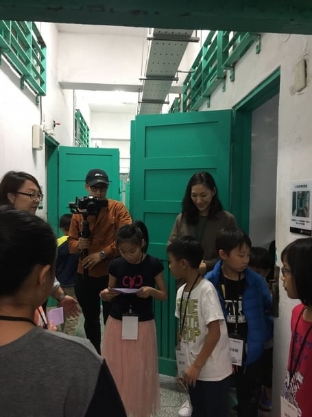 孩子在關押受難者的「押房」前演練解說內容。她對於狹小的空間、窺視內部的洞口和靠近地面設置的送飯小門印象深刻，認為這些設置是剝奪了人的隱私權和尊嚴。