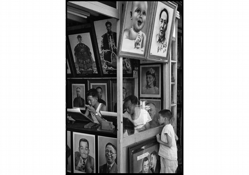 亨利．卡蒂爾－布列松（ Henri Cartier-Bresson），《在南市區的一間肖像畫舖子，作品不是實際寫真就是從相片臨摹。上海，1949年8月》（ Portrait painter’s shop in the Nan-Tao district. He works either from life or from a photograph. Shanghai, August 1949），銀鹽相紙，1949。（Courtesy of Fondation Henri Cartier-Bress