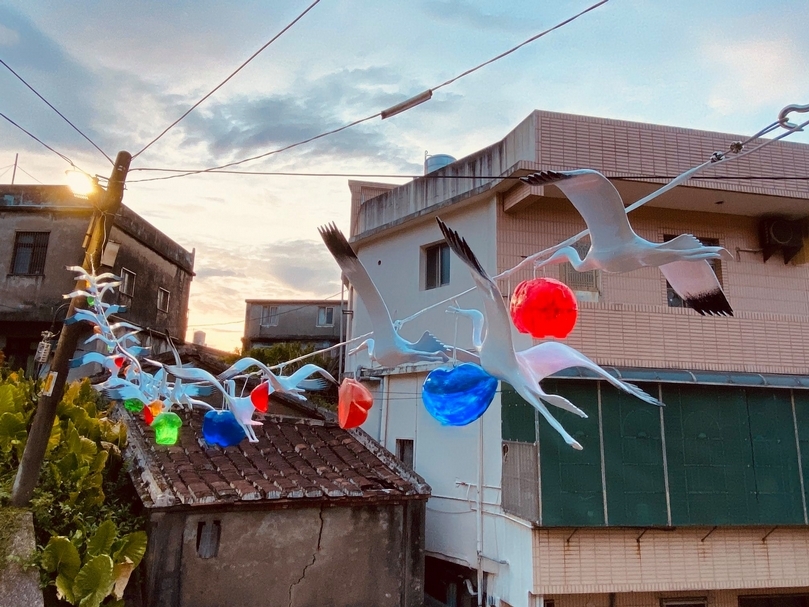由白鷺鷥帶著閃亮的幸福滿福包，寓意守護在地居民，也象徵著「啟航」揚帆遠颺。│簡俊成《幸福時光》