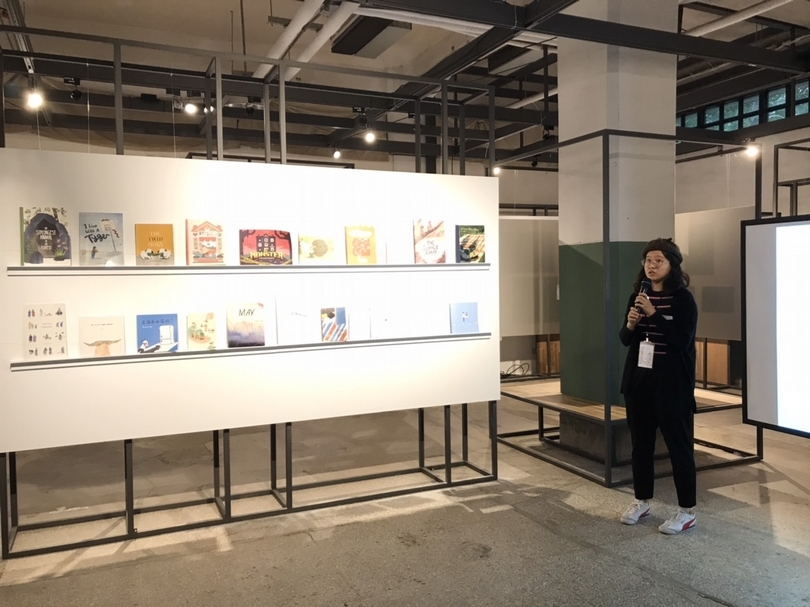 參展插畫家連心慈於開幕茶會介紹本次展覽緣起，旁邊展示插畫家未出版的圖畫書創作，期待有緣出版社慧眼合作。