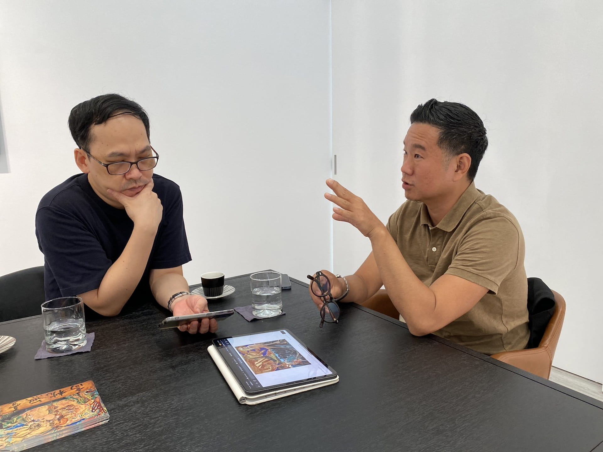 如果線條痕跡是陳建榮在繪畫裡的存在感，那麼一向在繪畫裡表現著強烈存在感的黨若洪，又是怎麼看近作裡的噴漆？圖為陳建榮（左）正看著手機裡的作品圖檔思考，黨若洪（右）則在講述自己的創作觀。（攝影／陳晞）