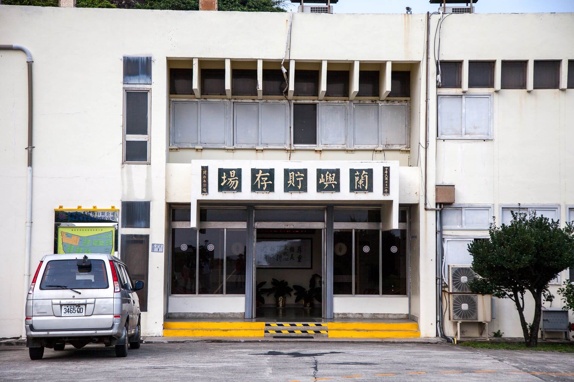 蘭嶼貯存場外觀。這張圖顯示出辦公大樓的正門口。該建物是由行政院國軍退除役官兵輔導委員會榮民工程事業管理處於1982年所興建，現為臺灣電力公司所有。（圖片來源：維基百科）
