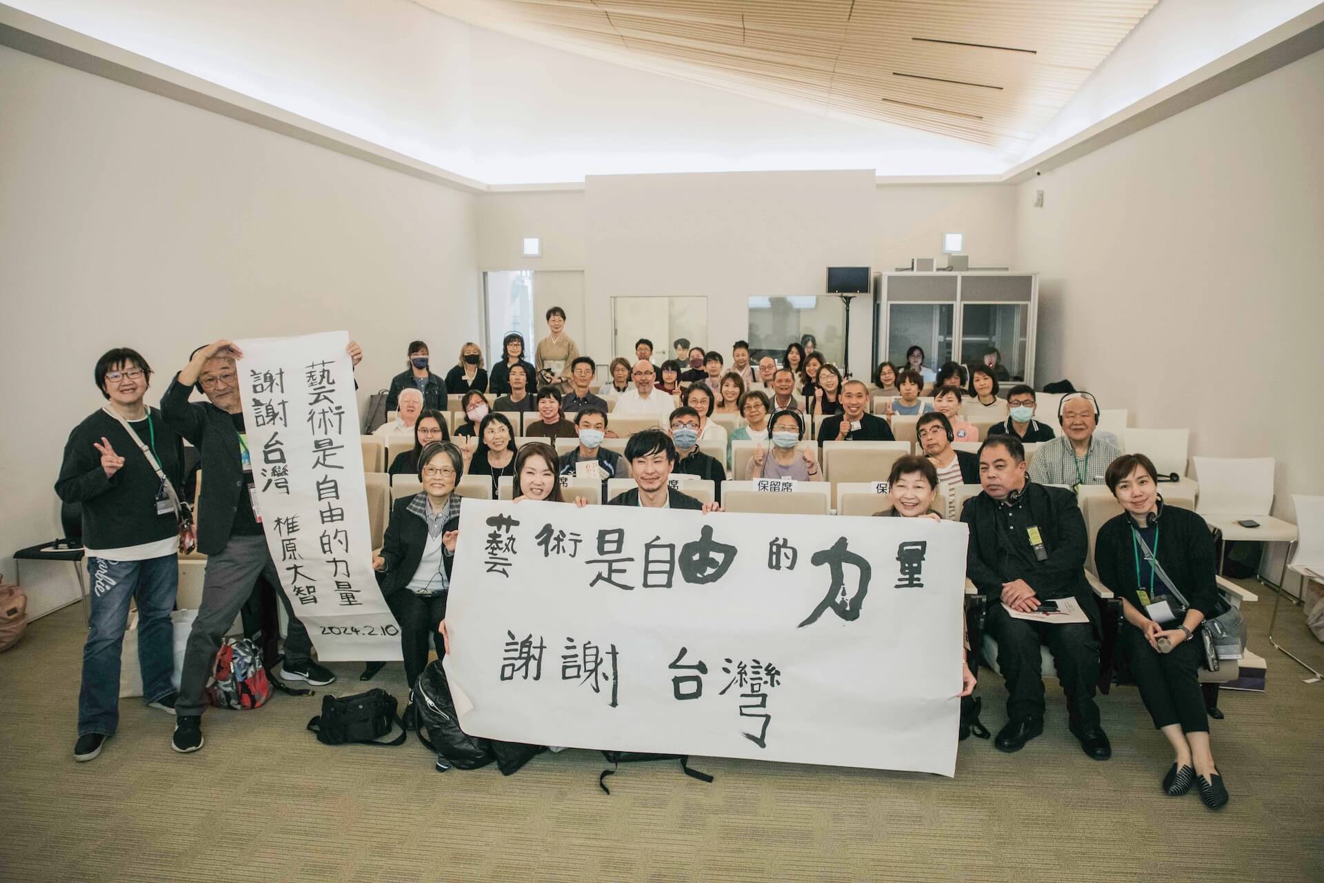 「臺灣×日本心智障礙者藝術發展國際交流論壇」第二日講者舉著本次「藝術是自由的力量」日本參展藝術家接力手寫的感謝手幅，與現場觀眾一同合影。（臺南市美術館提供）