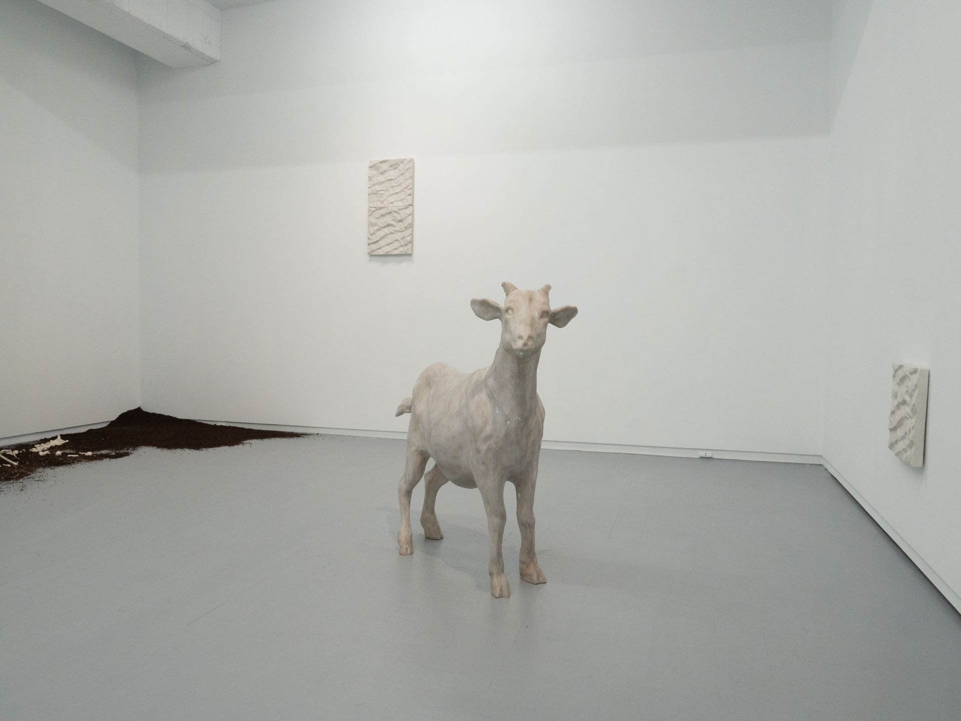 轉入展場則會看到站立在空間中以玻璃鋼翻製的羊《山羊》，還有在牆角的土堆中只剩下羊骨頭的《羊骨》。圖為「卡在鞋底的沙」展覽一隅，攝影／Kagaw Omin，谷公館提供