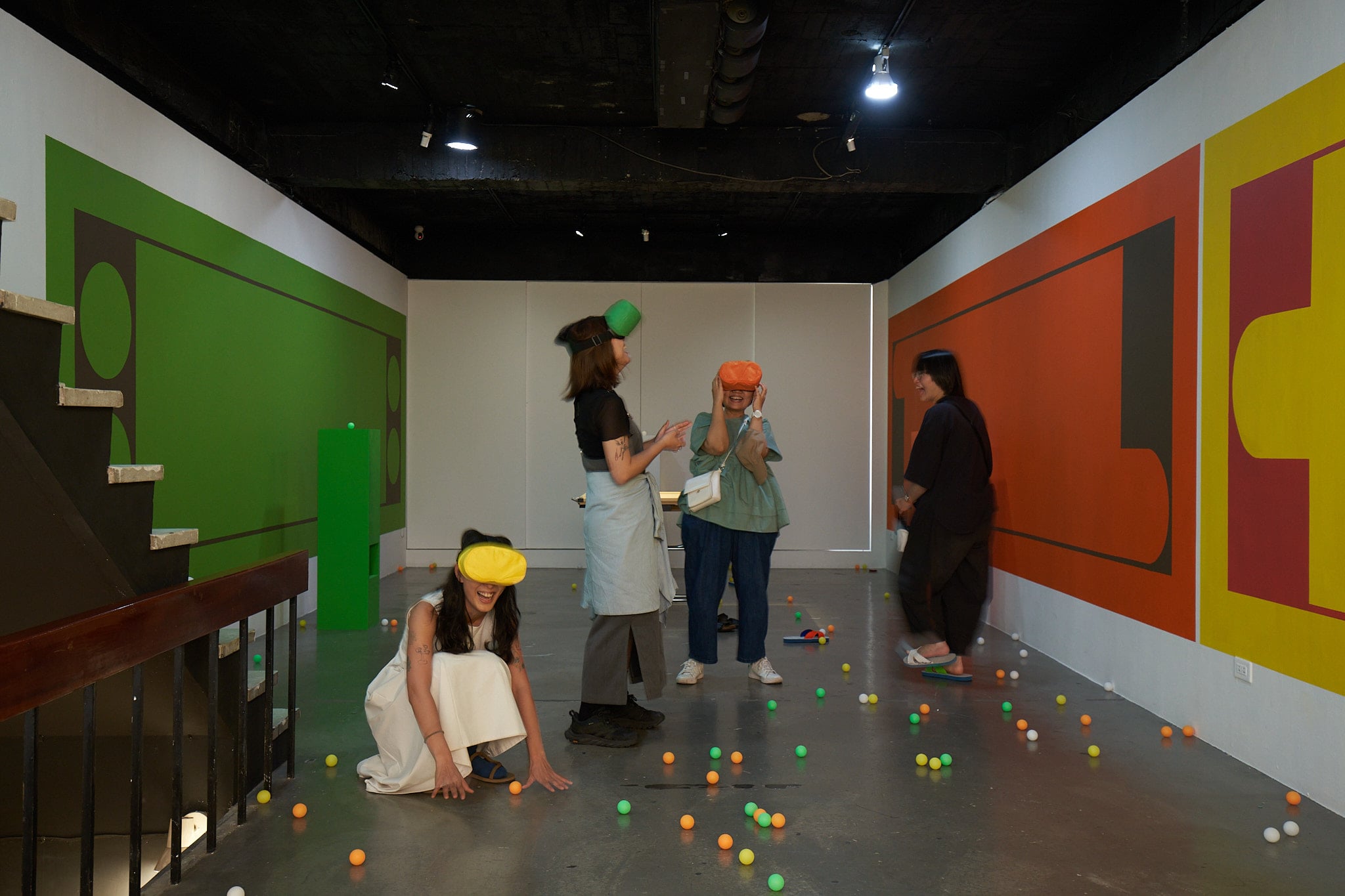 每一顏色的四色牌圖像前，皆放置著一個同樣色彩的木作直立展台，展台的頂部放置著該顏色的乒乓球，其內嵌的空間則有一個對應顏色的VR頭戴式裝置顯示器。圖為尹子潔個展「How Do You Do」展場。（沈裕融提供）