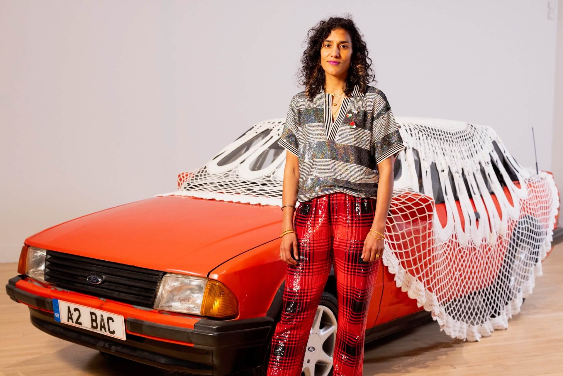 賈斯琳．考爾（Jasleen Kaur，1986-）與獲獎展覽「Alter Altar」作品覆蓋巨大傳統鉤編桌巾的鮮紅福特Escort汽車合影。（Credit David Parry, PA Media Assignments）