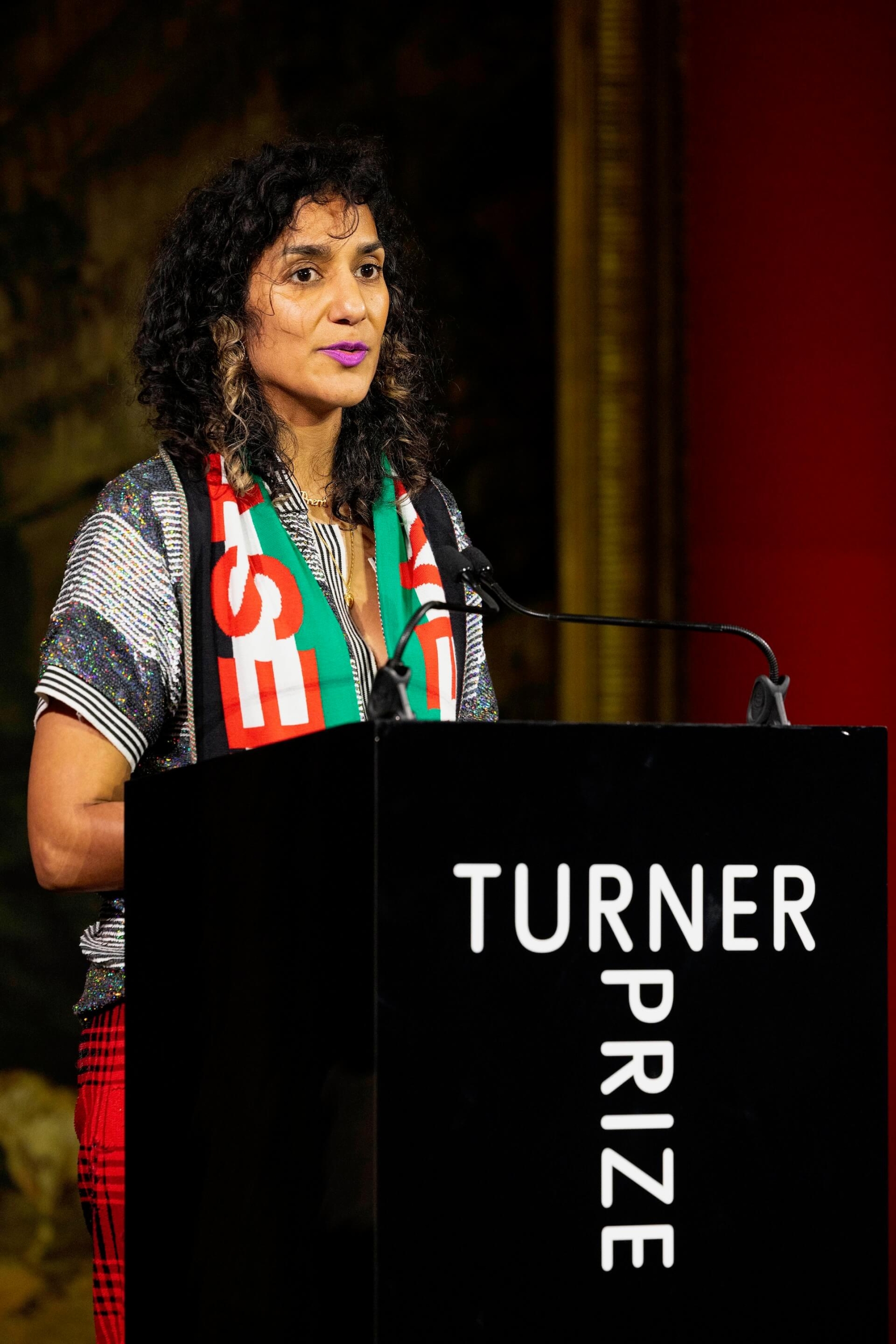 賈斯琳．考爾（Jasleen Kaur，1986-）身披巴勒斯坦國旗出席頒獎典禮，主張藝術家的政治表達應該被重視、呼籲以色列在加薩地區停火，並要求泰特美術館從她認為支持以色列政權的機構中撤資。（Credit David Parry, PA…