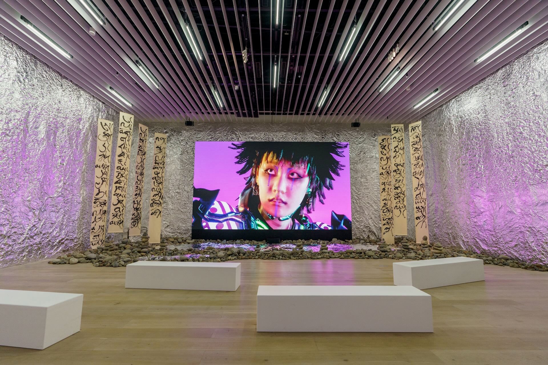 森美術館現場從天花板往下垂墜掛落陸揚的藏族老師之繪畫，以及在牆壁敷滿鋁箔，創造空間的雕塑感之餘，鋁箔的質地映照著螢幕之光亮，打造出陸揚的電玩佛教奇觀。圖為陸揚裝置作品展覽現場，攝影／Takehisa Naoki，森美術館提供。