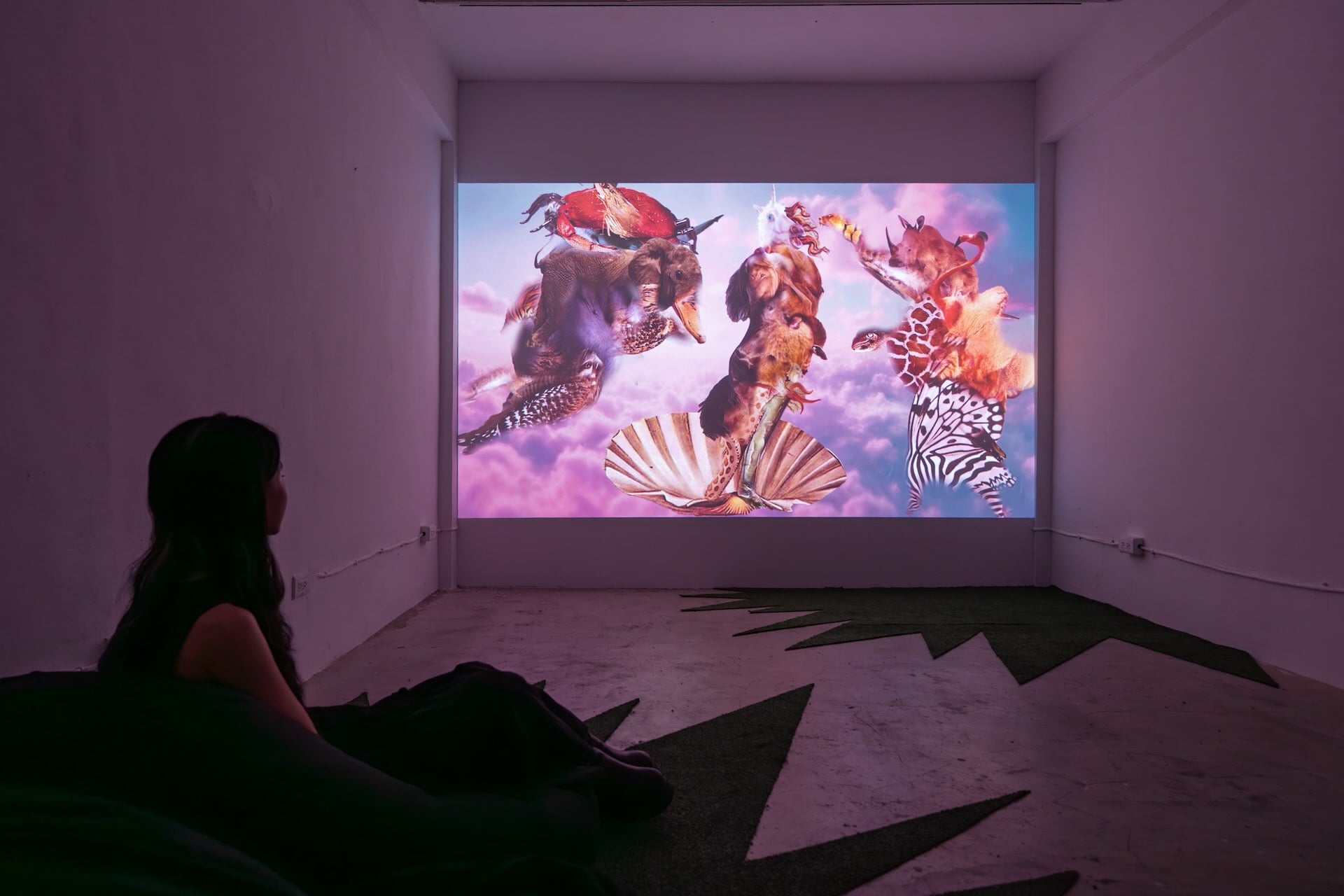 地下一樓展出的黃怡嘉《叢前叢前》，以單頻道錄像呈現，將進行曲旋律填詞為「YI JIA」音節，結合快速剪接與重複排列，串聯模仿動物或網路迷因的動作片段。參演者輪番變換角色，層層影像堆疊，營造出幽默又混亂的「怡嘉國度」。（攝影／劉耀鈞，介力屋提…