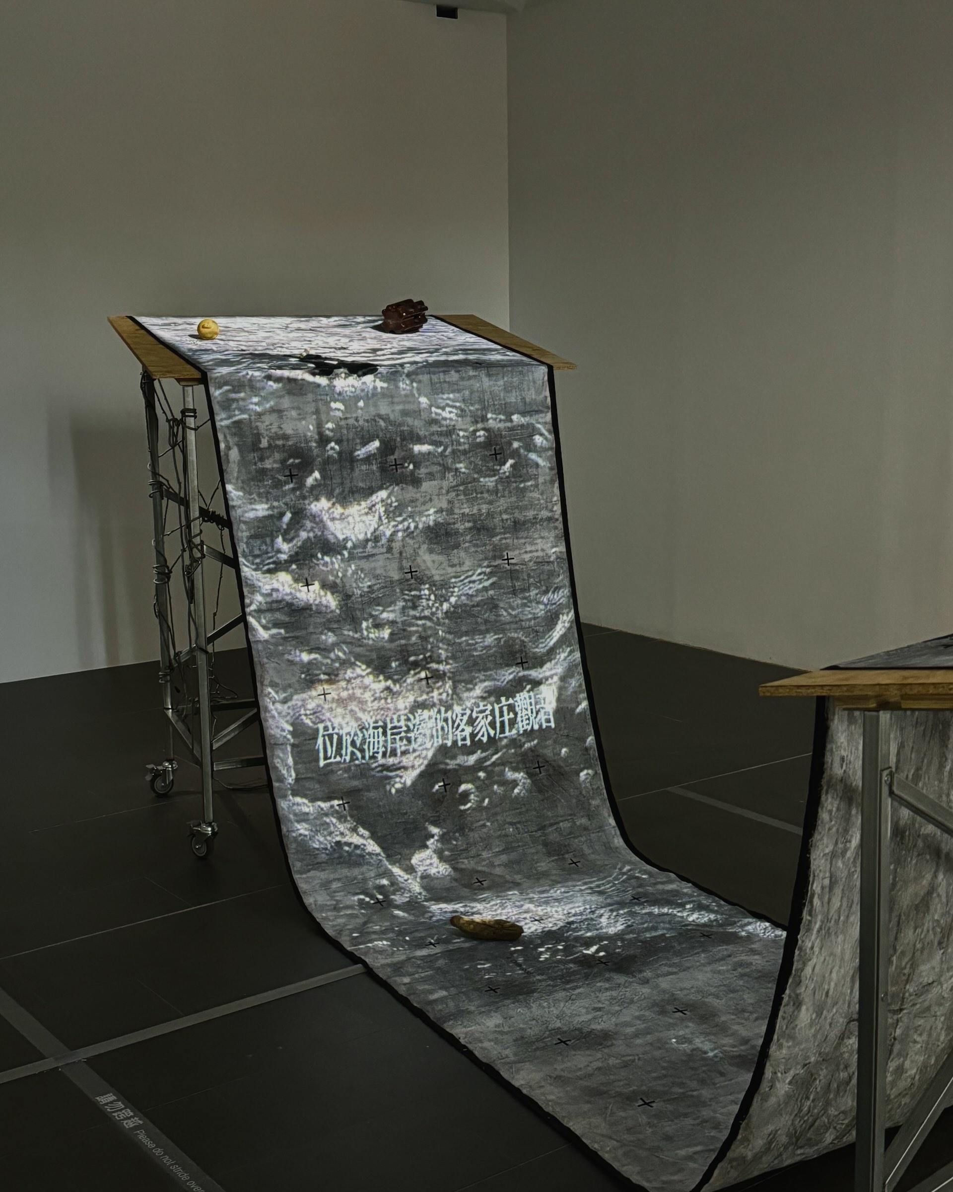 圖為張致中《暗湧》於「黑水」展出現場。作品以濕裝置結合潮汐影像與垂掛長布，承載藝術家對外祖父母跨海記憶的回望，將家族身分失語與情感暗流沉積於象徵歷史深處的「黑水」之中。（本刊資料室）