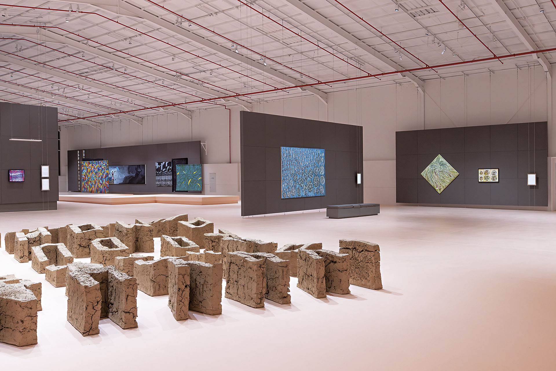 圖為2026年迪里耶當代藝術雙年展（Diriyah Contemporary Art Biennale）展覽現場「在插曲與過渡之中」一景：前景為展場裝置，右後方為皮歐．阿巴德（Pio Abad）《Vanwa》（2023/2026），左後方為…