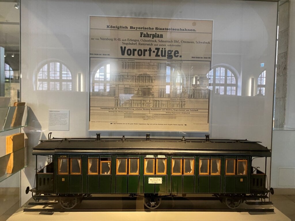 相｜這是一張1896年的時刻表和車廂模型。下方的車廂載運的，可以說是人類史上第一代的「通勤族」，當時他們要看著鐘錶，根據「中歐時間（MEZ）」在相片裡這些密密麻麻的城市裡通勤工作。我們可以在鐵道博物館裡，發現現代社會「時間秩序」的來源。