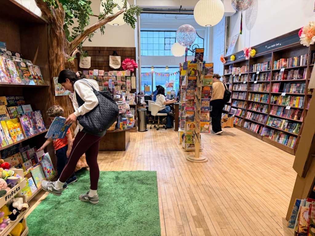 華倫街之字童書店從天花板垂吊下來的白色圓形大燈籠和亮片氣球，柔和了天花板的線條。書店中央有一棵紙糊的大樹，一旁書架上擺著科學類童書。