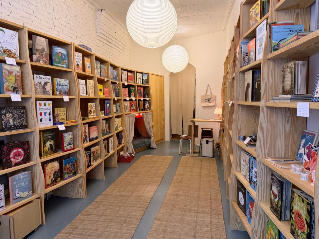 書店空間不大，但沿著左右牆壁擺放的淺色原木書架，和相同色系的擺設，讓空間看起來更明亮清新，且頗有精品店般的精緻感。大部分的書都是書封朝外擺放，也陳列著精選文具、美術用品和卡牌。有座書架的底層掛著布簾，拉開簾子，裡面居然有小沙發和燈，是可以讓…